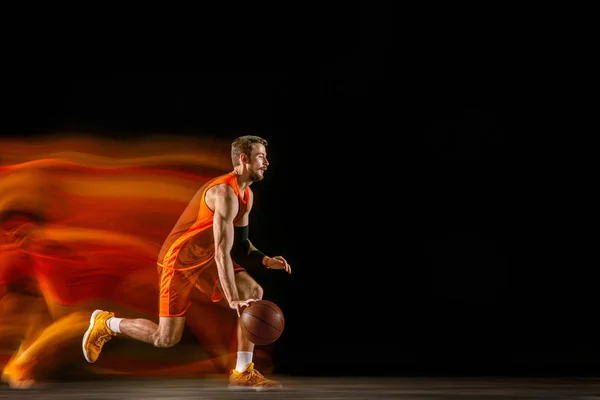 Jonge blanke basketballer tegen donkere achtergrond in gemengd licht — Stockfoto