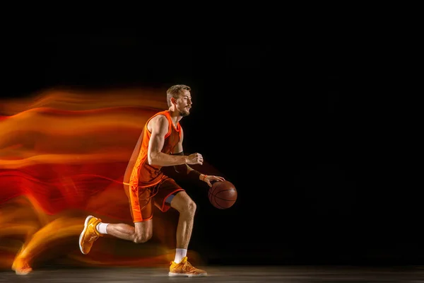 Jonge blanke basketballer tegen donkere achtergrond in gemengd licht — Stockfoto