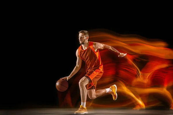 Young caucasian basketball player against dark background in mixed light — Stock Photo, Image