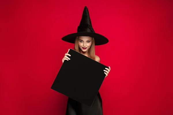 Mladá žena v klobouku jako čarodějka na červeném pozadí — Stock fotografie