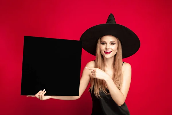 Mladá žena v klobouku jako čarodějka na červeném pozadí — Stock fotografie