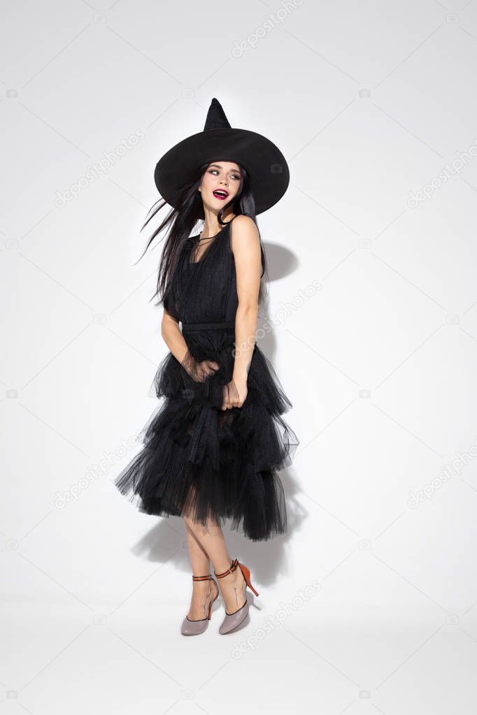 Young woman in hat and dress as a witch on white background