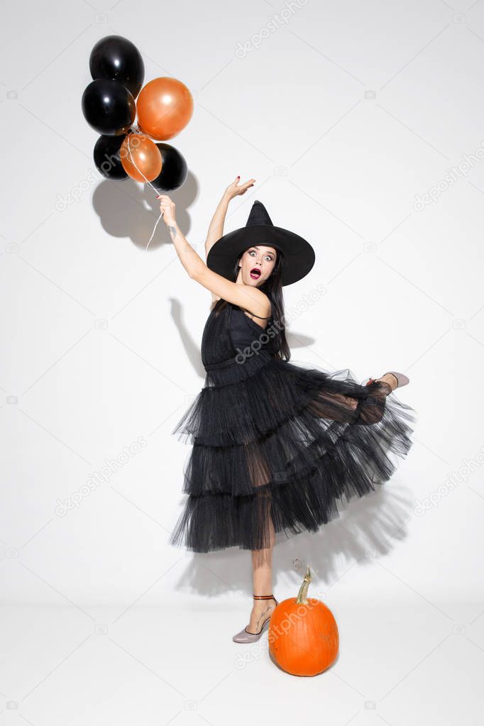 Young woman in hat and dress as a witch on white background