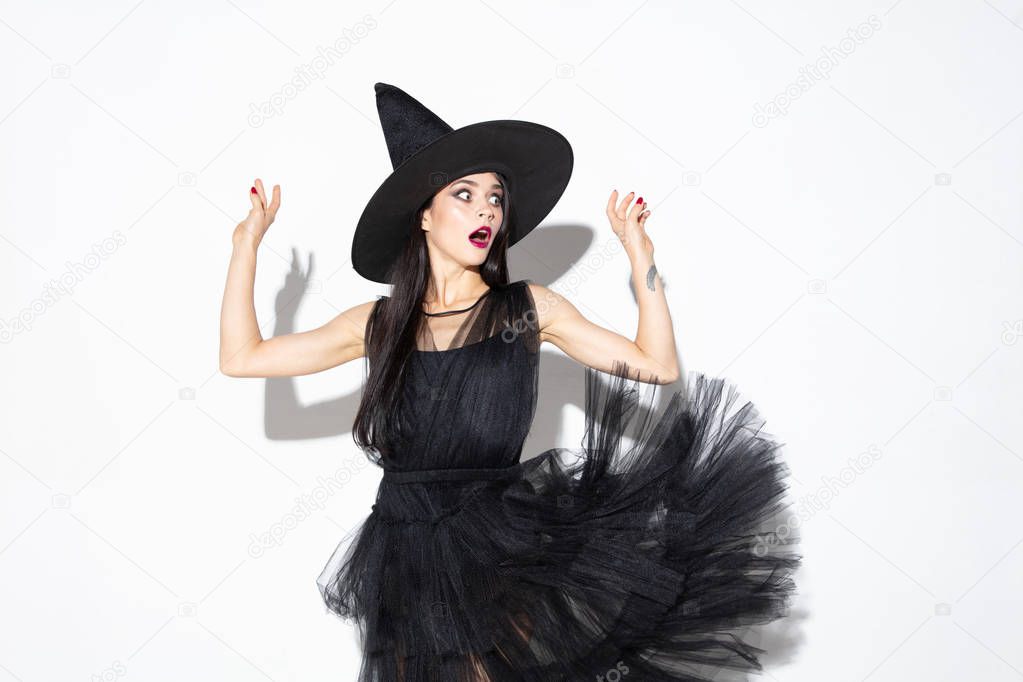 Young woman in hat and dress as a witch on white background