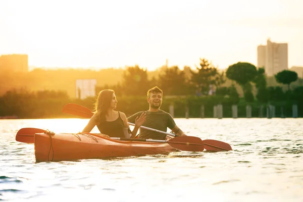 Selbstbewusstes junges Paar beim Kajakfahren auf dem Fluss mit Sonnenuntergang im Hintergrund — Stockfoto