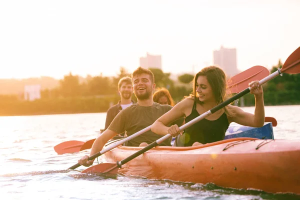 Heureux amis kayak sur la rivière avec coucher de soleil sur le fond — Photo