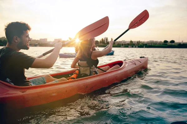 Pasangan muda yang percaya diri kayak di sungai bersama dengan matahari terbenam di latar belakang — Stok Foto