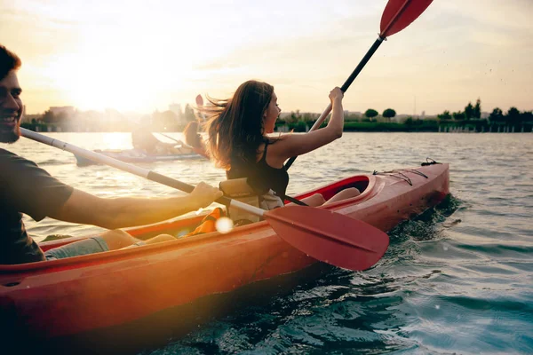 Confident young couple kayaking on river together with sunset on the background — Stock Photo, Image
