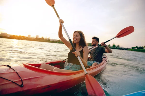 Confident young couple kayaking on river together with sunset on the background — Stock Photo, Image