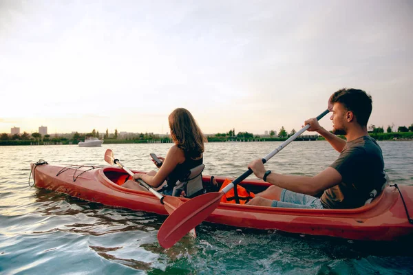 Confident young couple kayaking on river together with sunset on the background — Stock Photo, Image