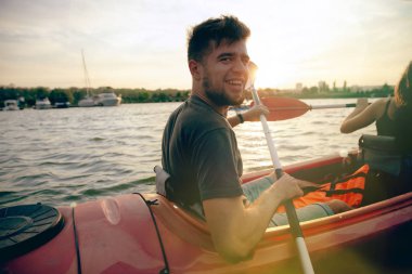 Kendinden emin genç çift arka planda gün batımı ile birlikte nehir üzerinde kayak