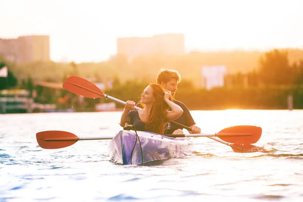 Selbstbewusstes junges Paar beim Kajakfahren auf dem Fluss mit Sonnenuntergang im Hintergrund — Stockfoto