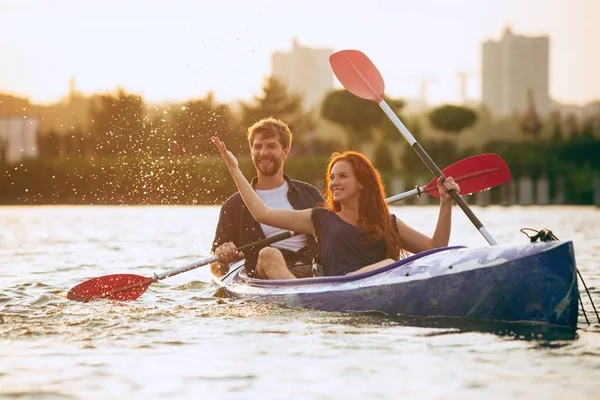 Confident young couple kayaking on river together with sunset on the background — Stock Photo, Image