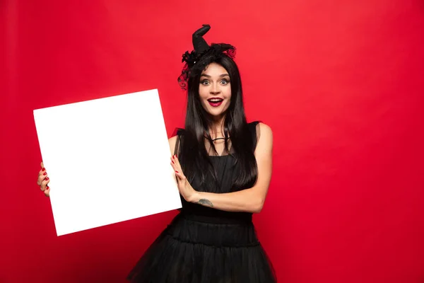 Jovem mulher de chapéu e vestido como uma bruxa no fundo vermelho — Fotografia de Stock