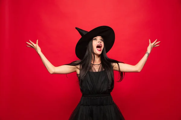 Mladá žena v klobouku a oblékat se jako čarodějka na červeném pozadí — Stock fotografie