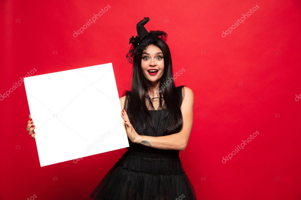 Young woman in hat and dress as a witch on red background