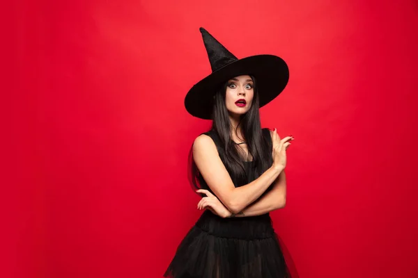 Mujer joven con sombrero y vestido de bruja sobre fondo rojo —  Fotos de Stock