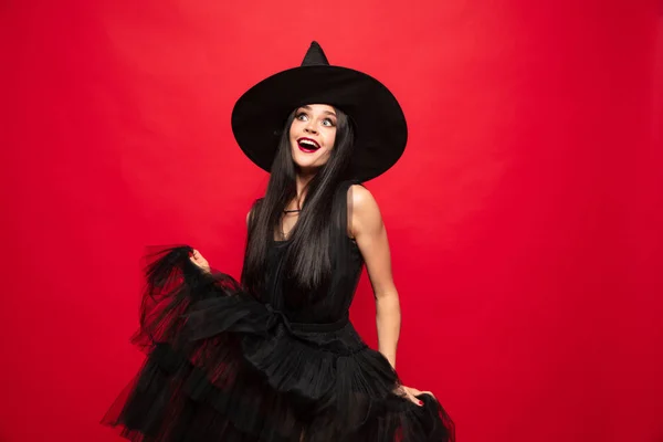 Mujer joven con sombrero y vestido de bruja sobre fondo rojo — Foto de Stock