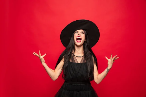 Jonge vrouw in muts en jurk als een heks op rode achtergrond — Stockfoto