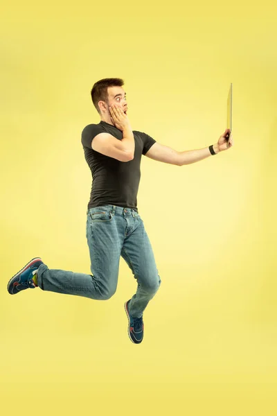 Retrato de comprimento total de homem de salto feliz com gadgets no fundo amarelo — Fotografia de Stock