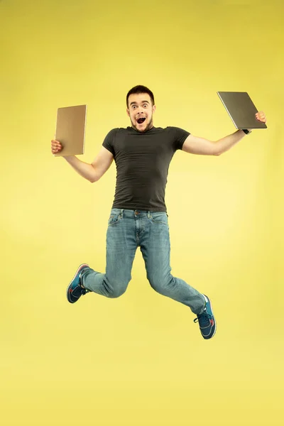 Full length portrait of happy jumping man with gadgets on yellow background — Stock Photo, Image