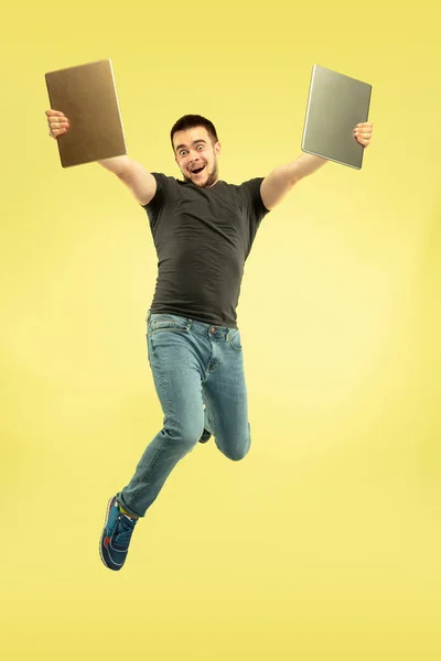 Full length portrait of happy jumping man with gadgets on yellow background — Stock Photo, Image