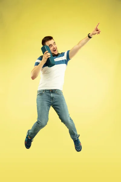 Full length portrait of happy jumping man with gadgets on yellow background — Stock Photo, Image