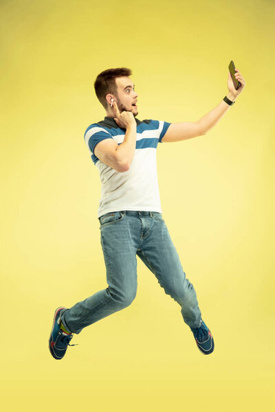 Full length portrait of happy jumping man with gadgets on yellow background