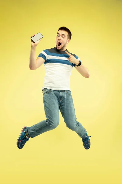 Портрет щасливого стрибаючого чоловіка з гаджетами на жовтому тлі — стокове фото