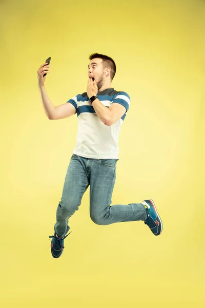 Портрет щасливого стрибаючого чоловіка з гаджетами на жовтому тлі — стокове фото