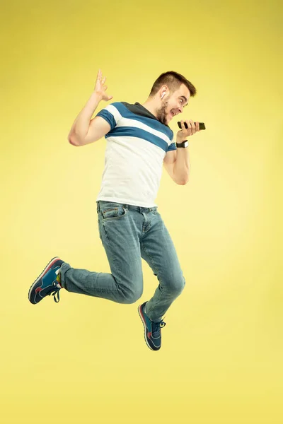 Retrato de longitud completa del hombre saltando feliz con gadgets sobre fondo amarillo — Foto de Stock