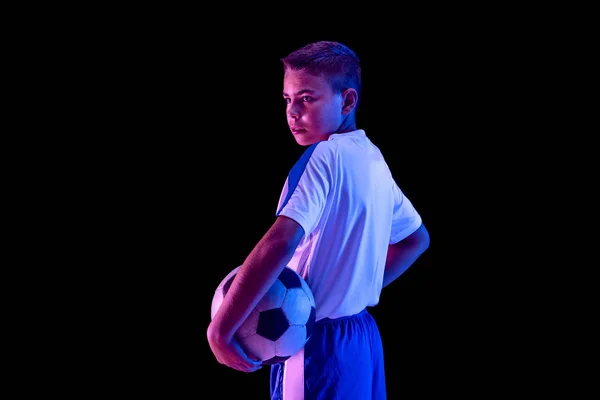Młody chłopak jako piłkarz lub piłkarz na tle ciemnego studia — Zdjęcie stockowe