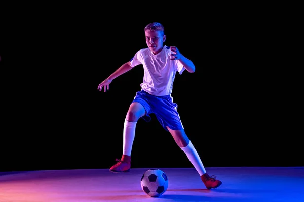 Fiatal fiú, mint egy foci, vagy focista a sötét stúdió háttérben — Stock Fotó