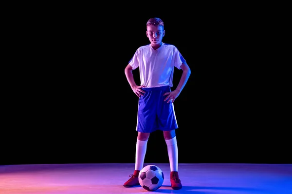 年轻的男孩作为一个足球或足球运动员在黑暗的工作室背景 — 图库照片