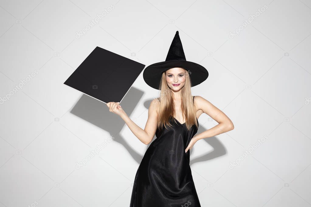 Young woman in hat as a witch on white background