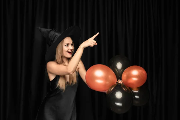 Mladá žena v klobouku jako čarodějka na černém pozadí — Stock fotografie