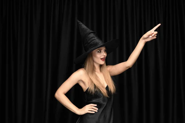 Mujer joven en sombrero como una bruja sobre fondo negro —  Fotos de Stock