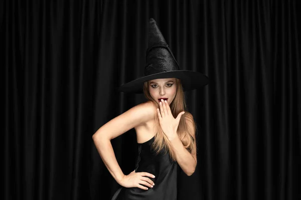 Молодая женщина в шляпе как ведьма на черном фоне — стоковое фото