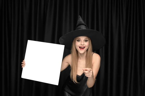 Mladá žena v klobouku jako čarodějka na černém pozadí — Stock fotografie
