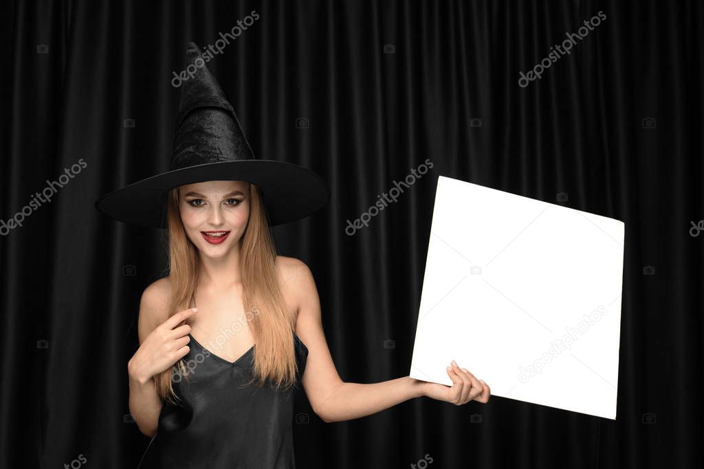 Young woman in hat as a witch on black background