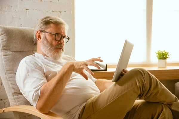 Старший чоловік, який працює з планшетом вдома концепція домашнього навчання — стокове фото