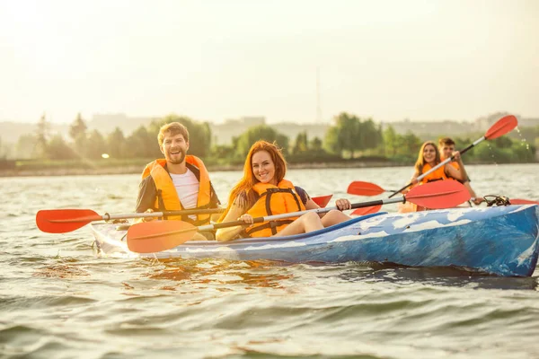 Lyckliga vänner kajakpaddling på floden med solnedgång på bakgrunden — Stockfoto