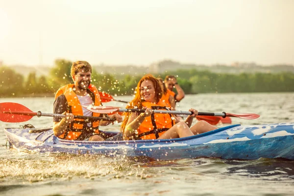 Amici felici kayak sul fiume con il tramonto sullo sfondo — Foto Stock