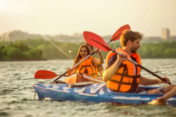 Heureux amis kayak sur la rivière avec coucher de soleil sur le fond — Photo