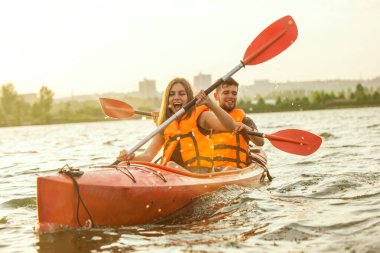 Mutlu çift nehirde kayak yapıyor, arka planda günbatımı var.