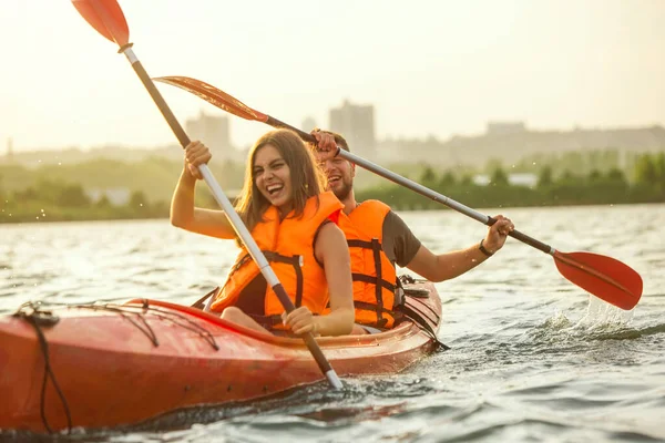 Casal feliz de caiaque no rio com o pôr do sol no fundo — Fotografia de Stock