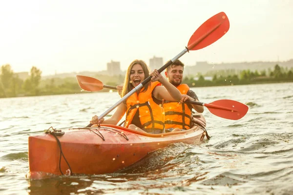 Glückliches Paar beim Kajakfahren auf dem Fluss mit Sonnenuntergang im Hintergrund — Stockfoto