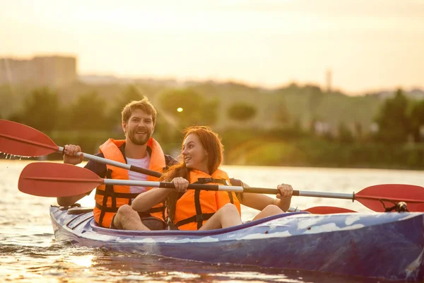 Happy couple kayaking on river with sunset on the background — Stock Photo, Image