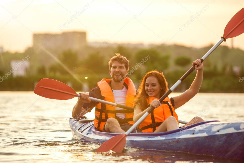Happy couple kayaking on river with sunset on the background