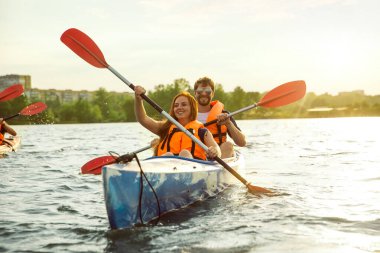 Mutlu çift nehirde kayak yapıyor, arka planda günbatımı var.